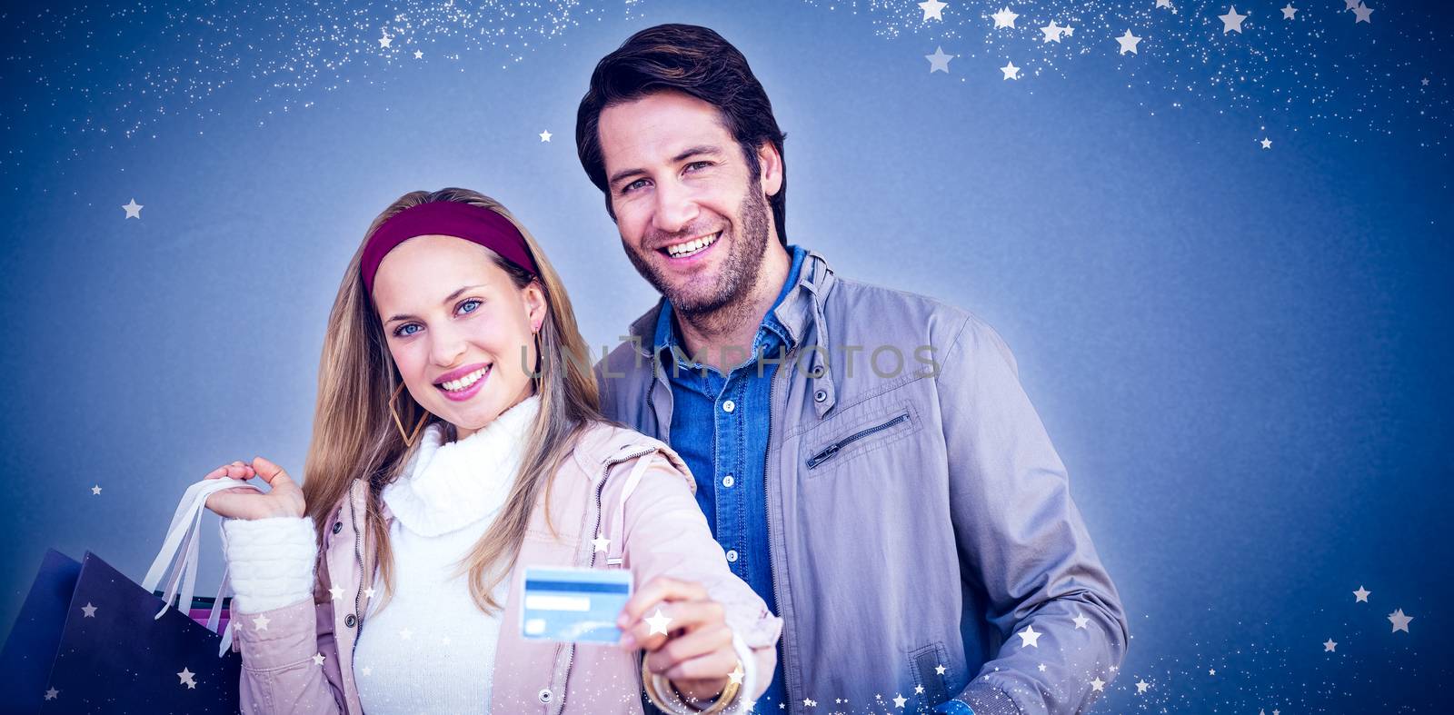 Smiling couple with shopping bags showing credit card against blue background