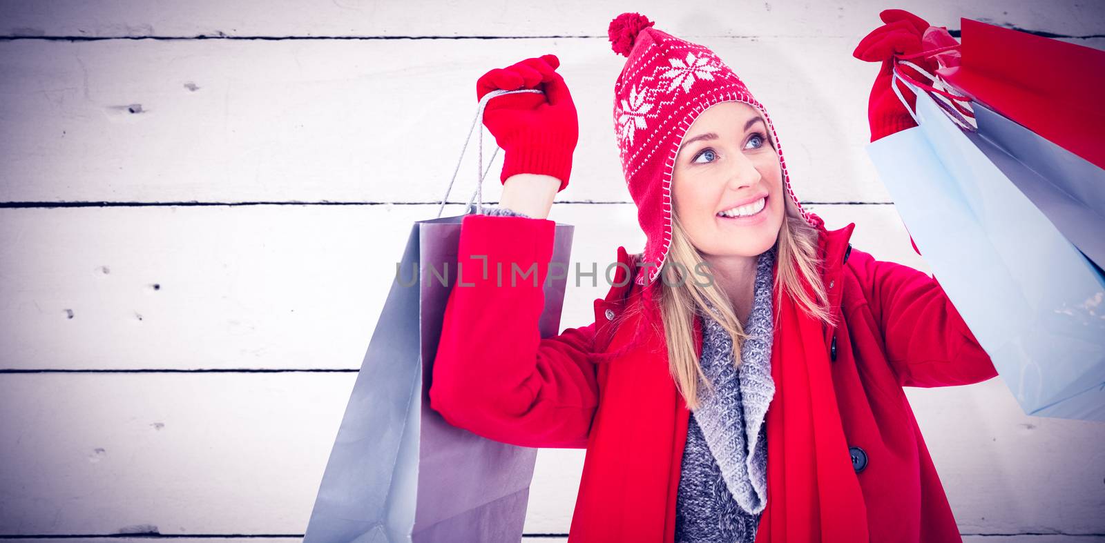 Blonde in winter clothes holding shopping bags against white wood