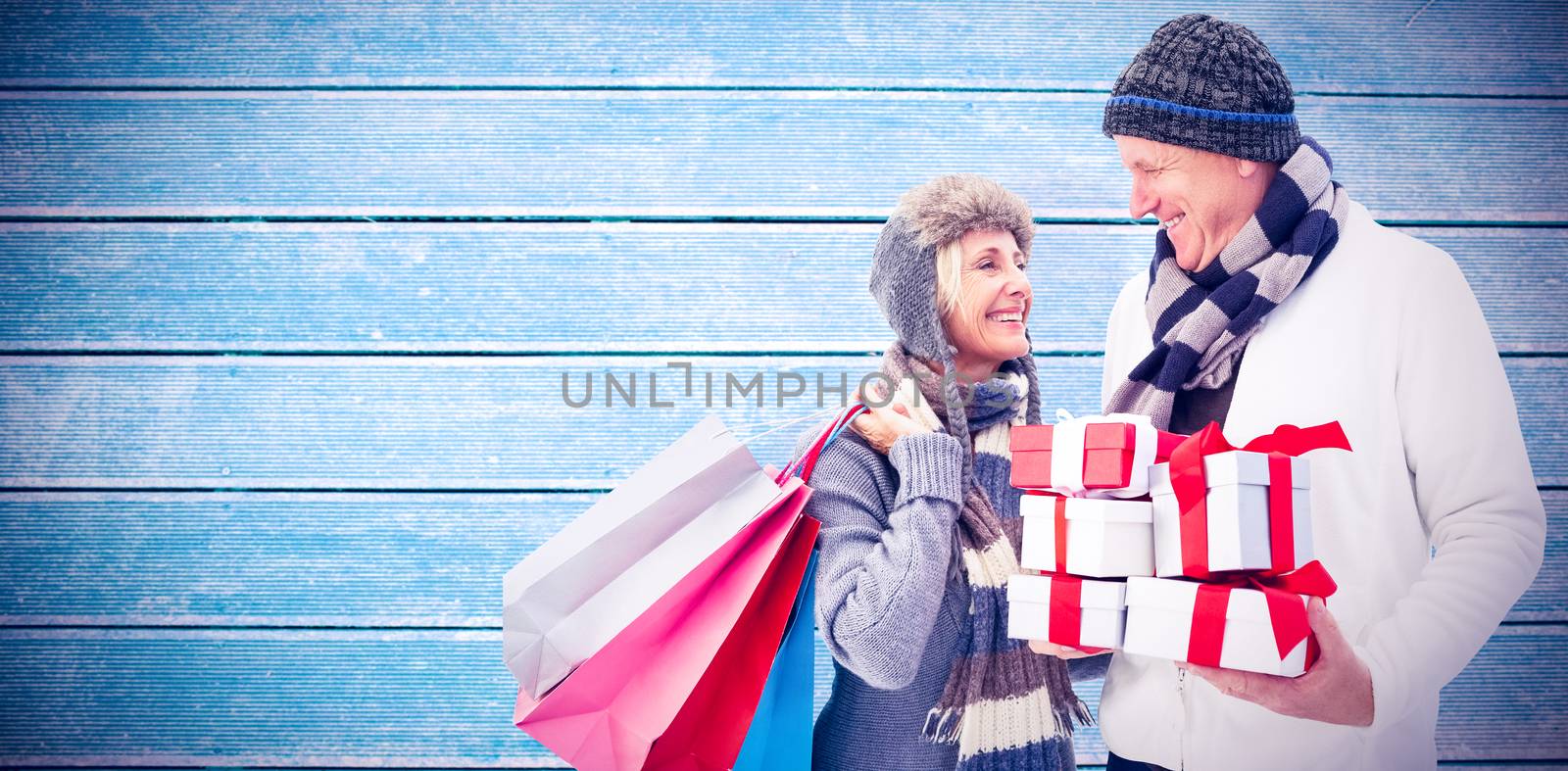 Festive mature couple holding christmas gifts against wooden planks