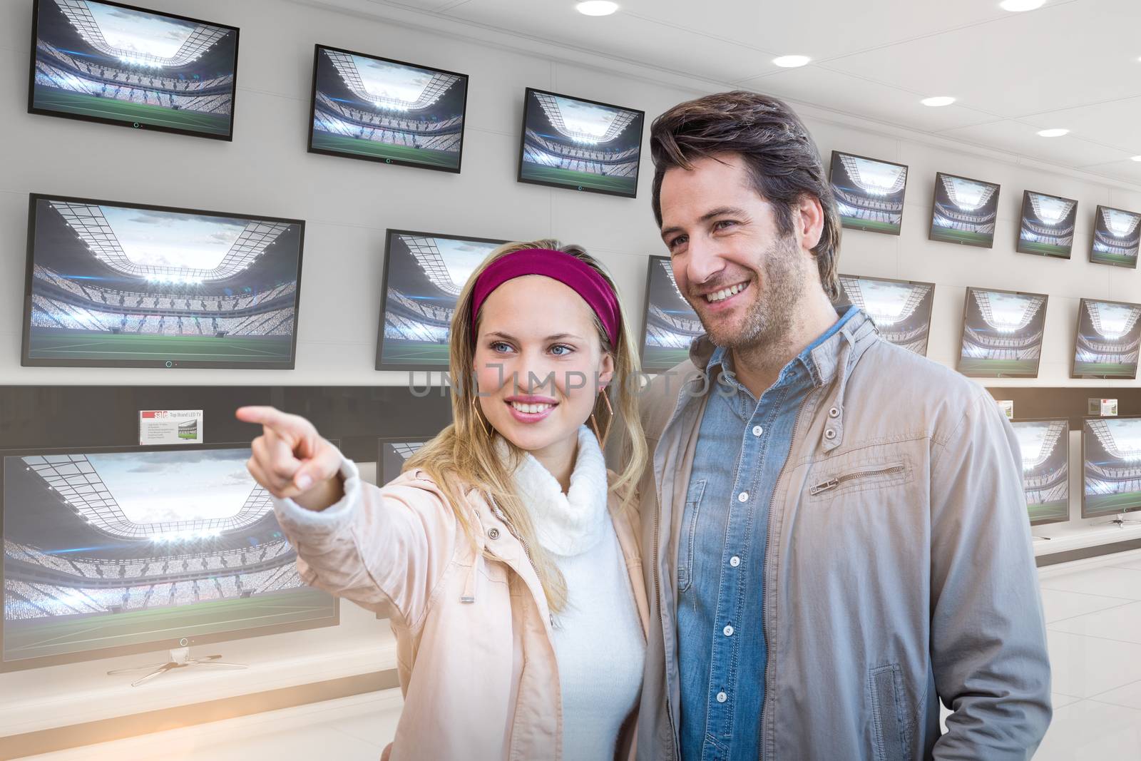 Smiling couple looking and pointing against televisions for sale