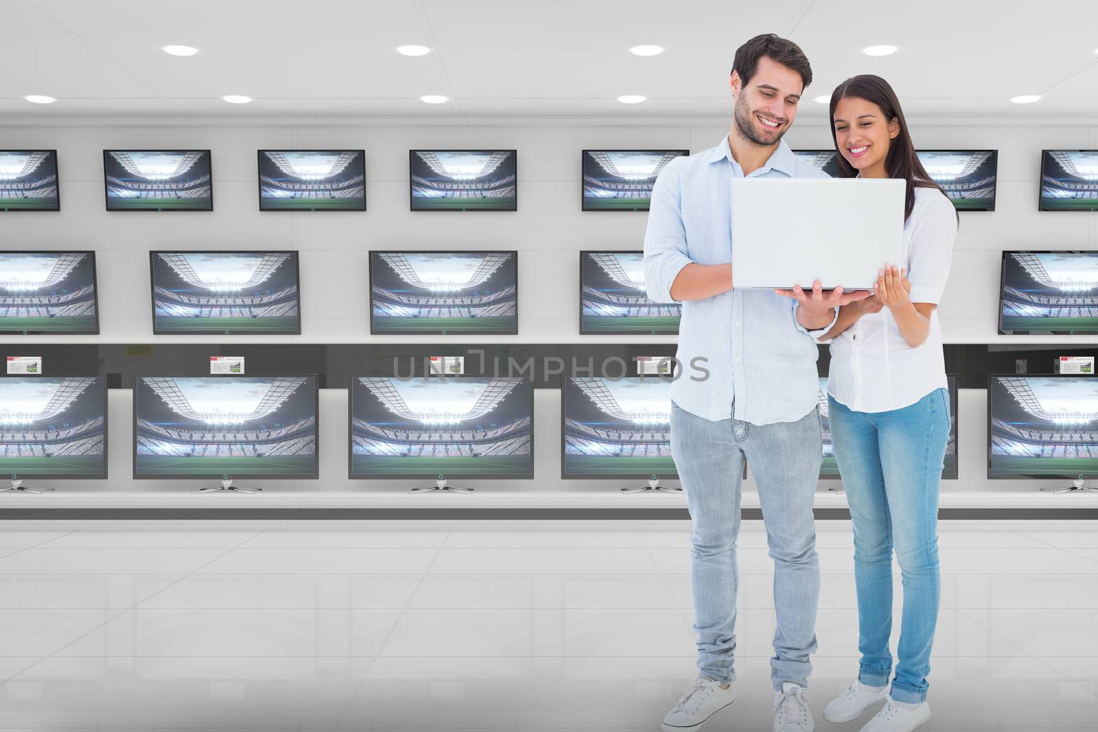 Attractive young couple holding their laptop against televisions for sale