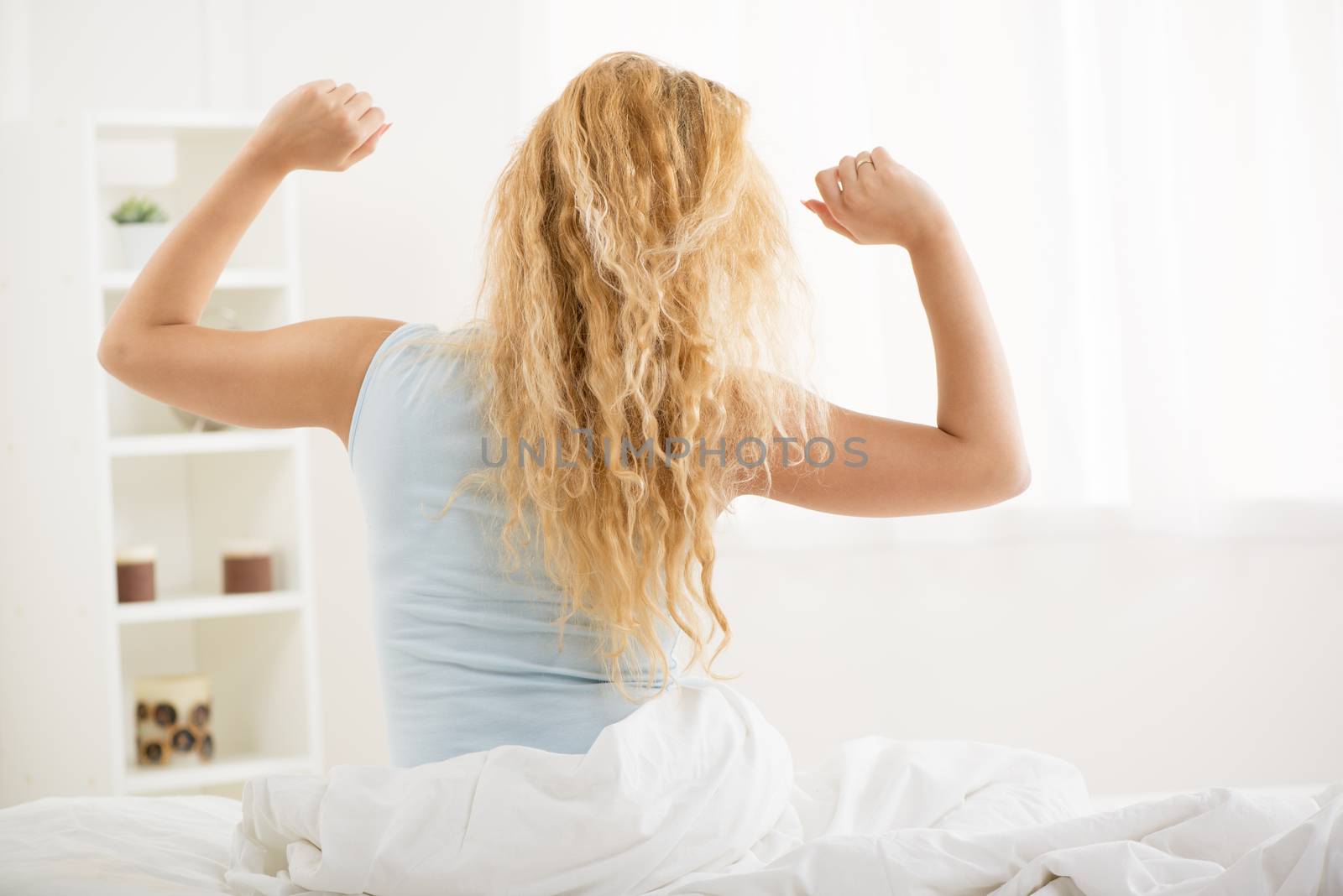 Cute young woman awakening in the morning. She is stretching in the bed. Rear view