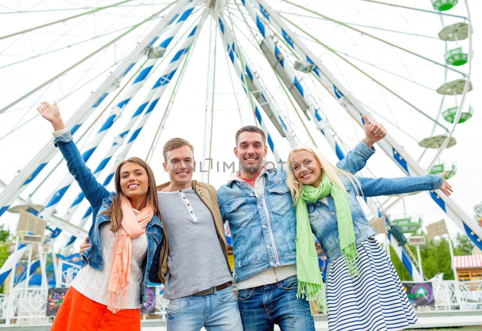 leisure, amusement park and friendship concept - group of smiling friends waving hands with ferris wheel on the back