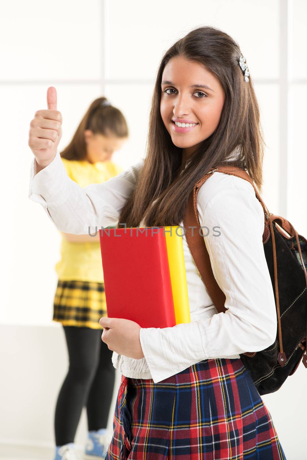 Happy beautiful teenage girl with Colorful books and school bag showing thumbs up