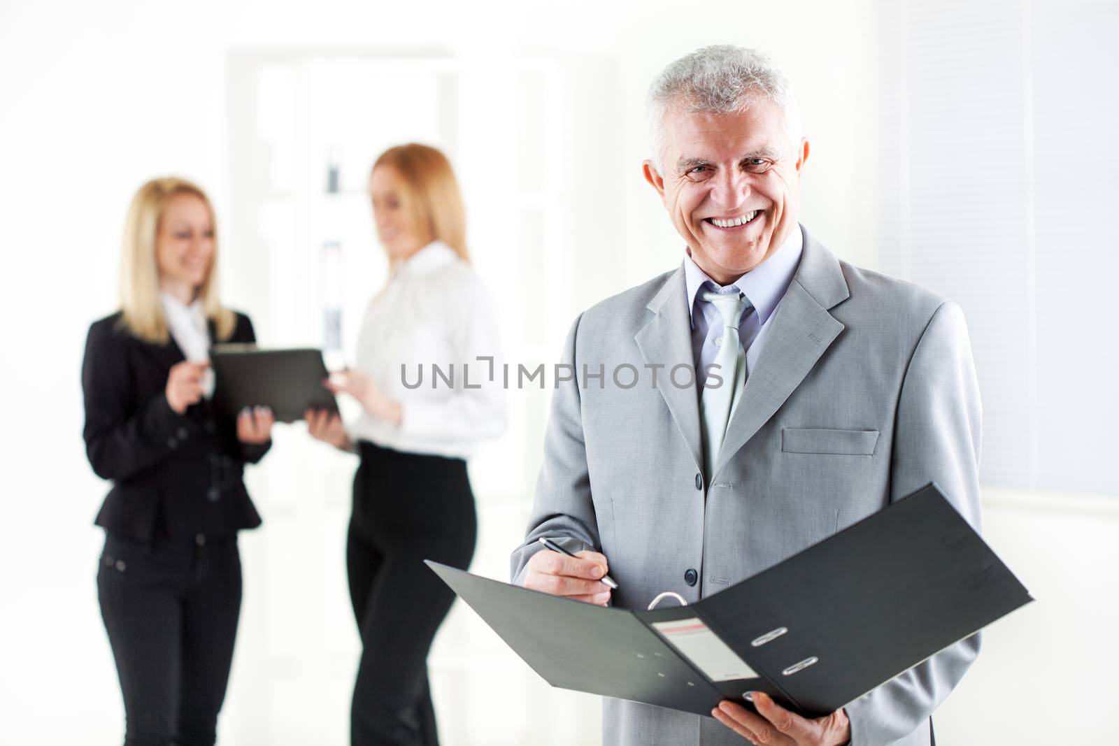 Happy senior businessman with folder standing in the office. Looking at camera. Selective Focus. 