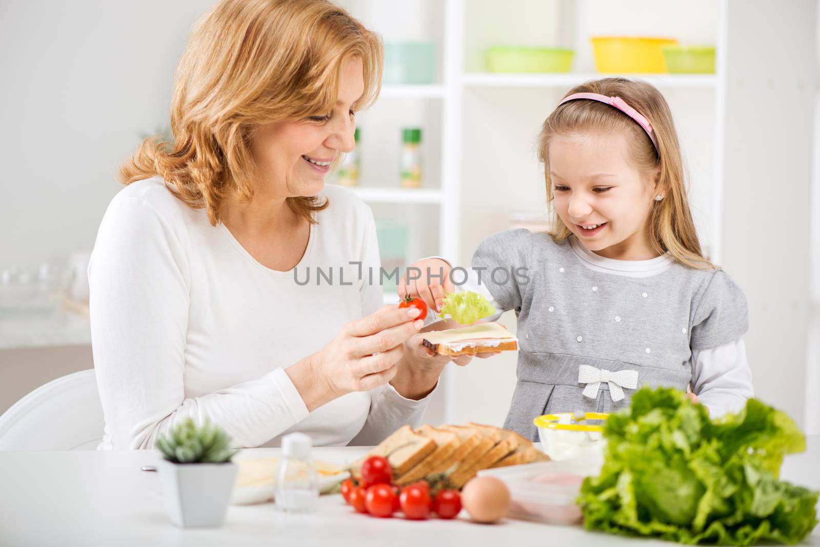 Cute little girl with Grandmother making a Sandwich in the kitchen.