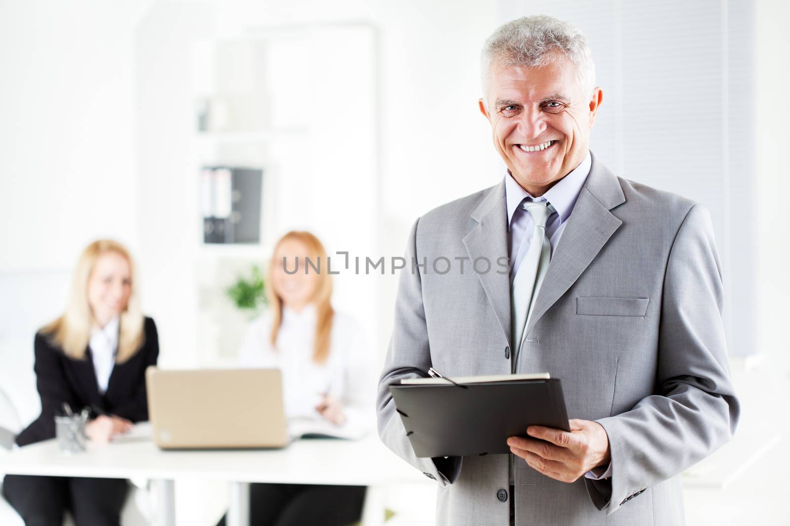 Happy senior businessman with documents standing in the office. Looking at camera. Selective Focus.