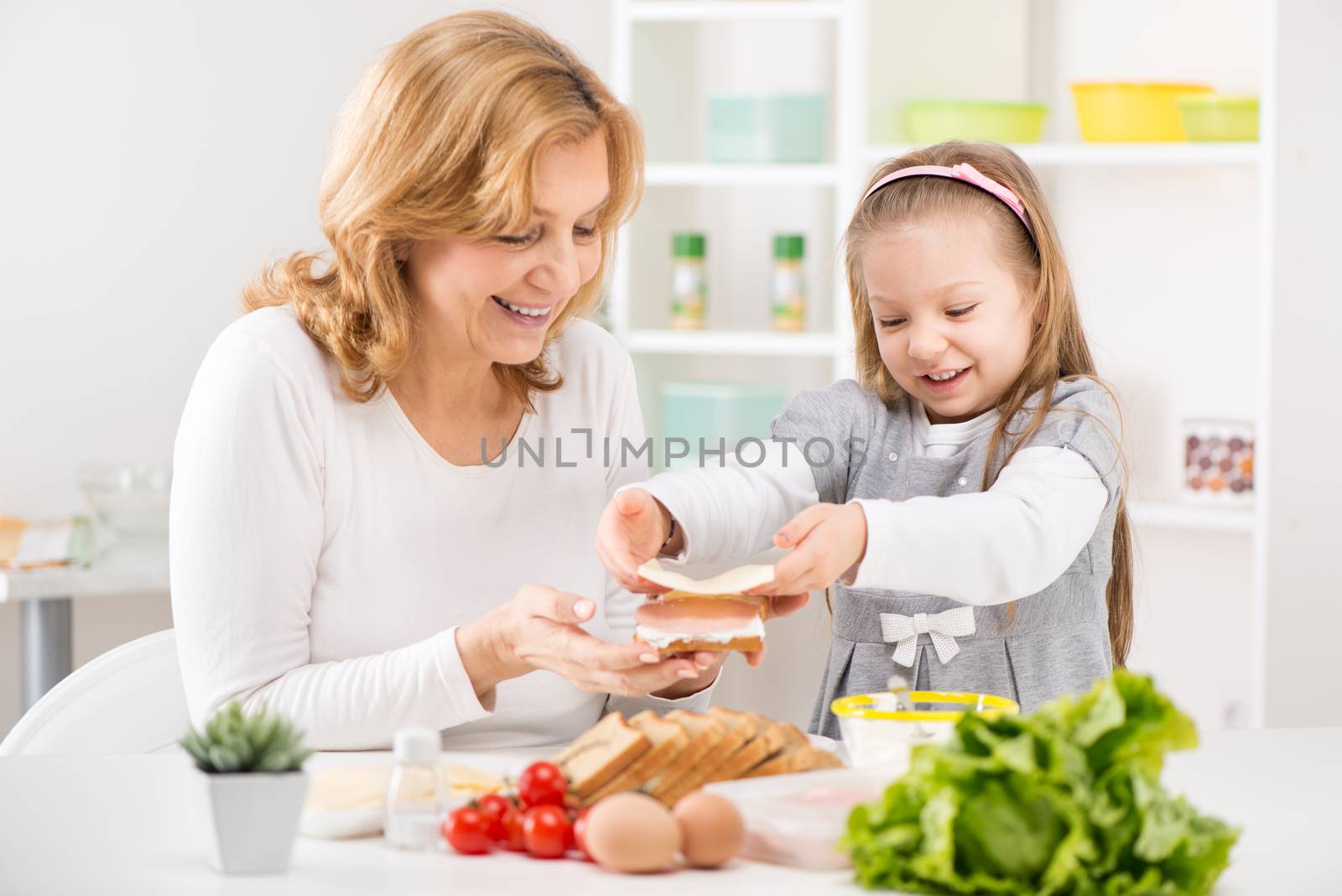 Cute little girl with Grandmother making a Sandwich in the kitchen.