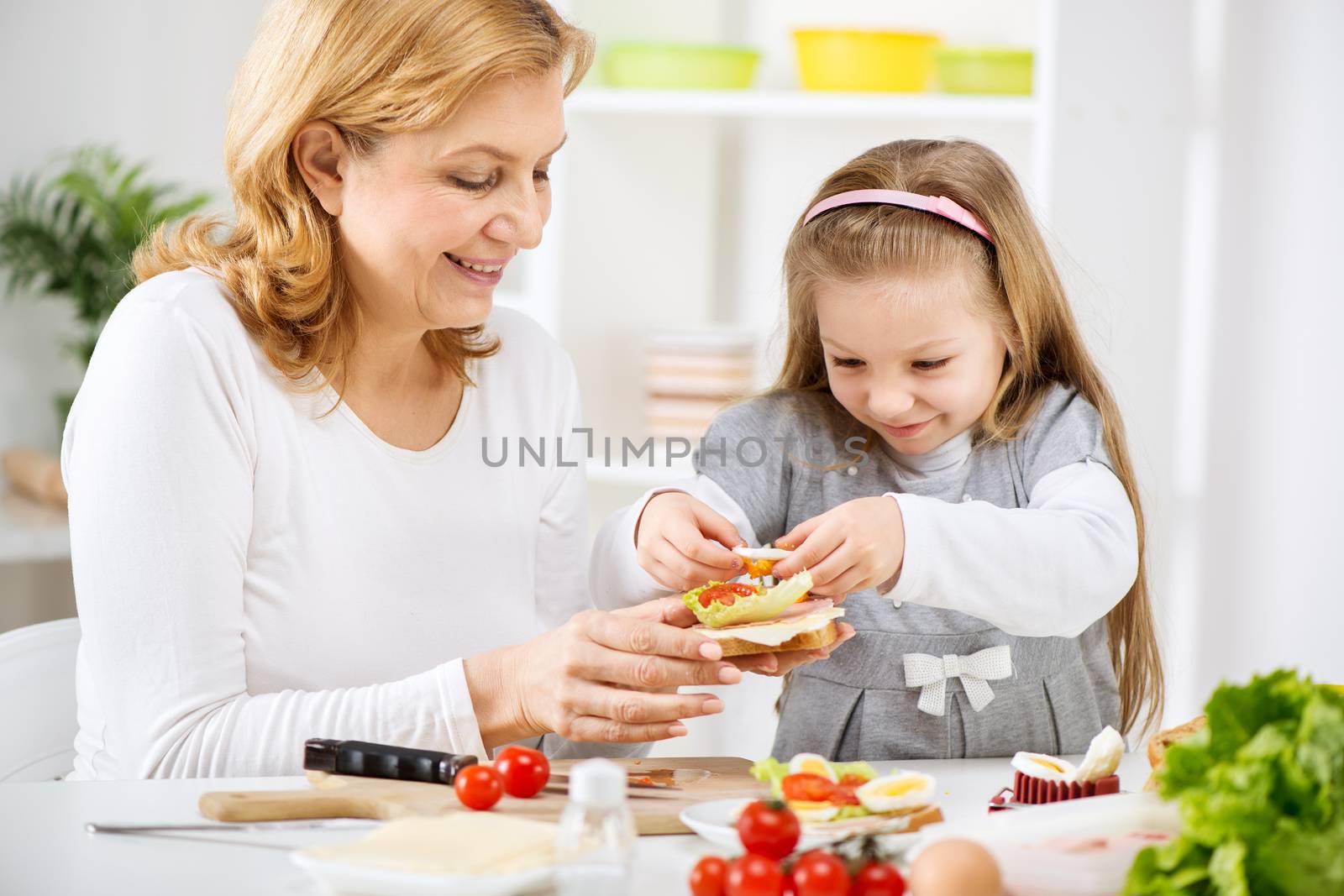Beautiful happy grandmother and her cute granddaughter making a Sandwich in the kitchen.