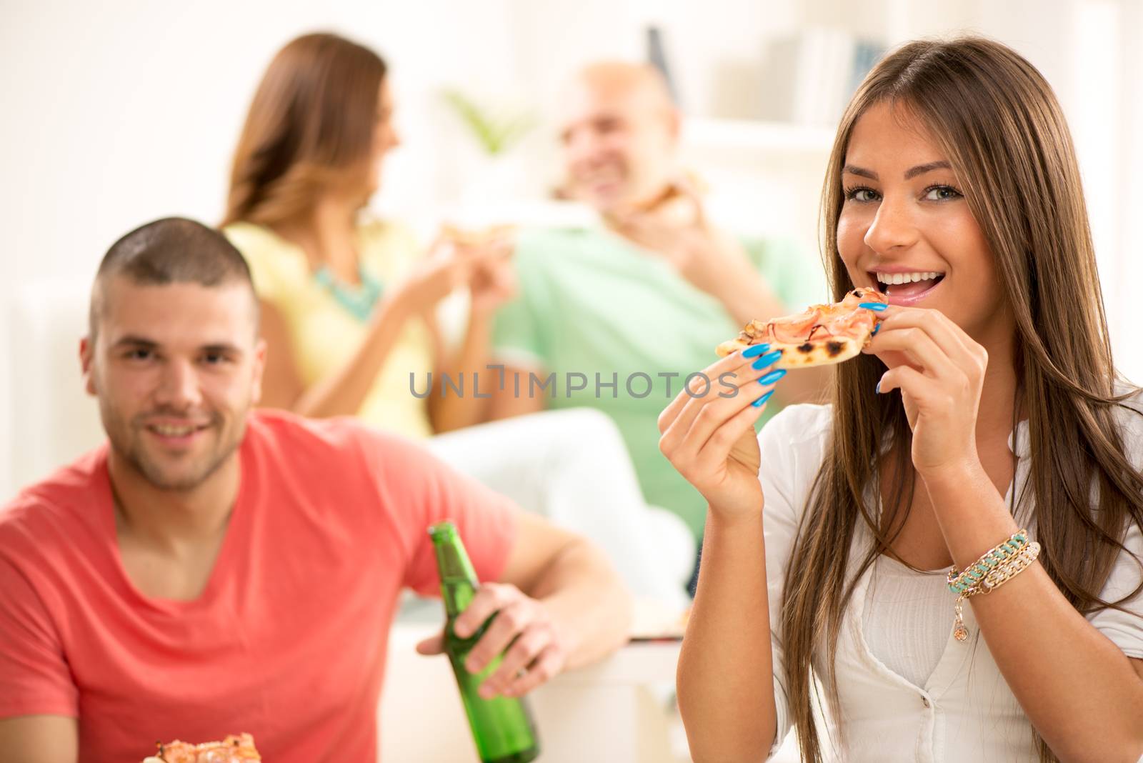 Close up of a young girl smiling and eating pizza with her friends in the background.