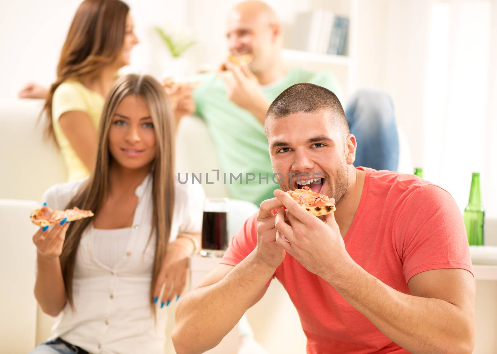 Close up of a young men smiling and eating pizza with her friends in the background.