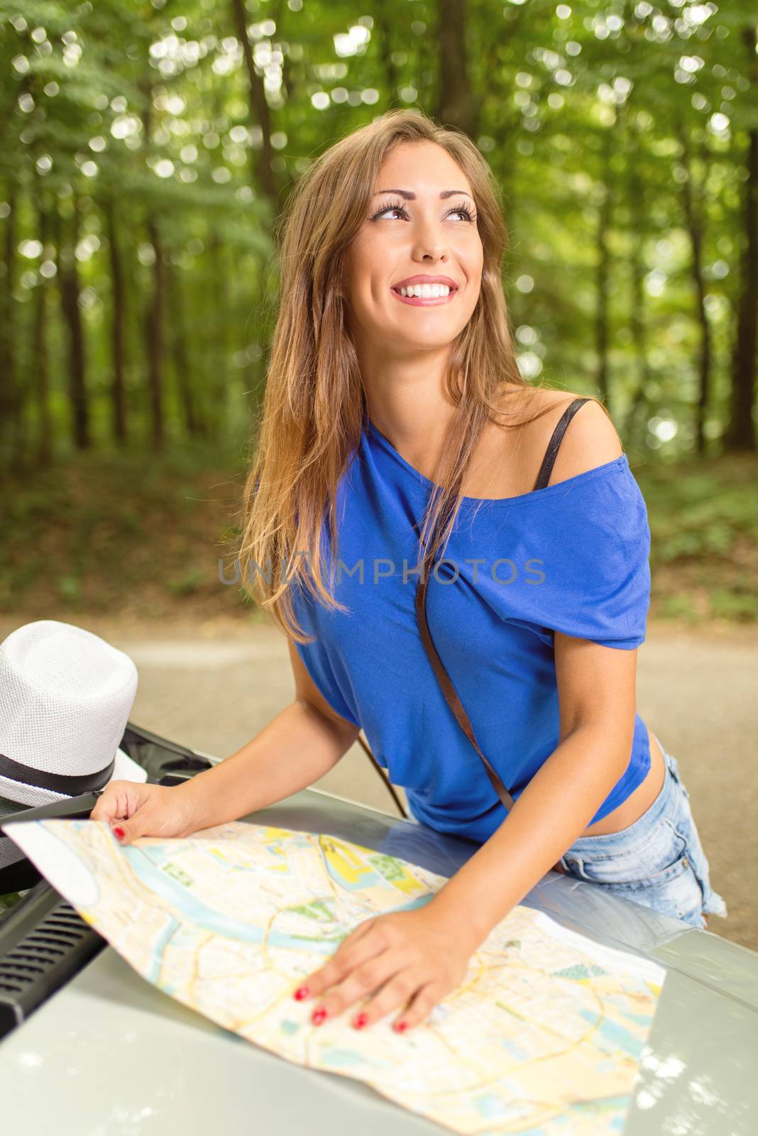 Young beautiful woman standing before a car in the forest, holding map and looking at destination.