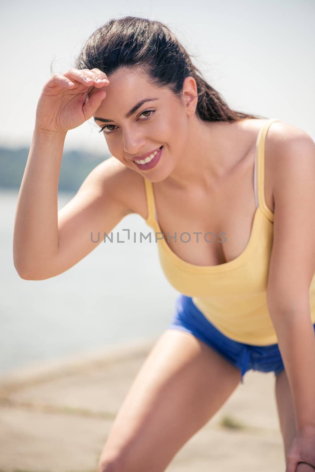 Beautiful young woman resting after jogging by the river and wipes the sweat from his forehead.