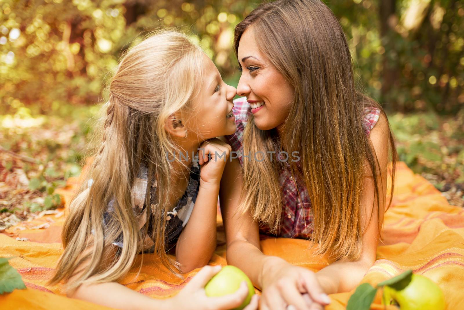 It's the autumn season and beautiful mom and her little girl is lying in a forest full of autumn leaves and enjoying. 