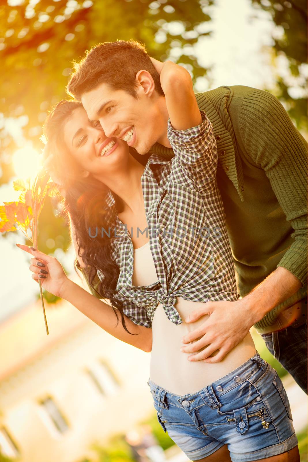 Young love couple in the park are embraced, a girl carries sprig of autumn leaves.