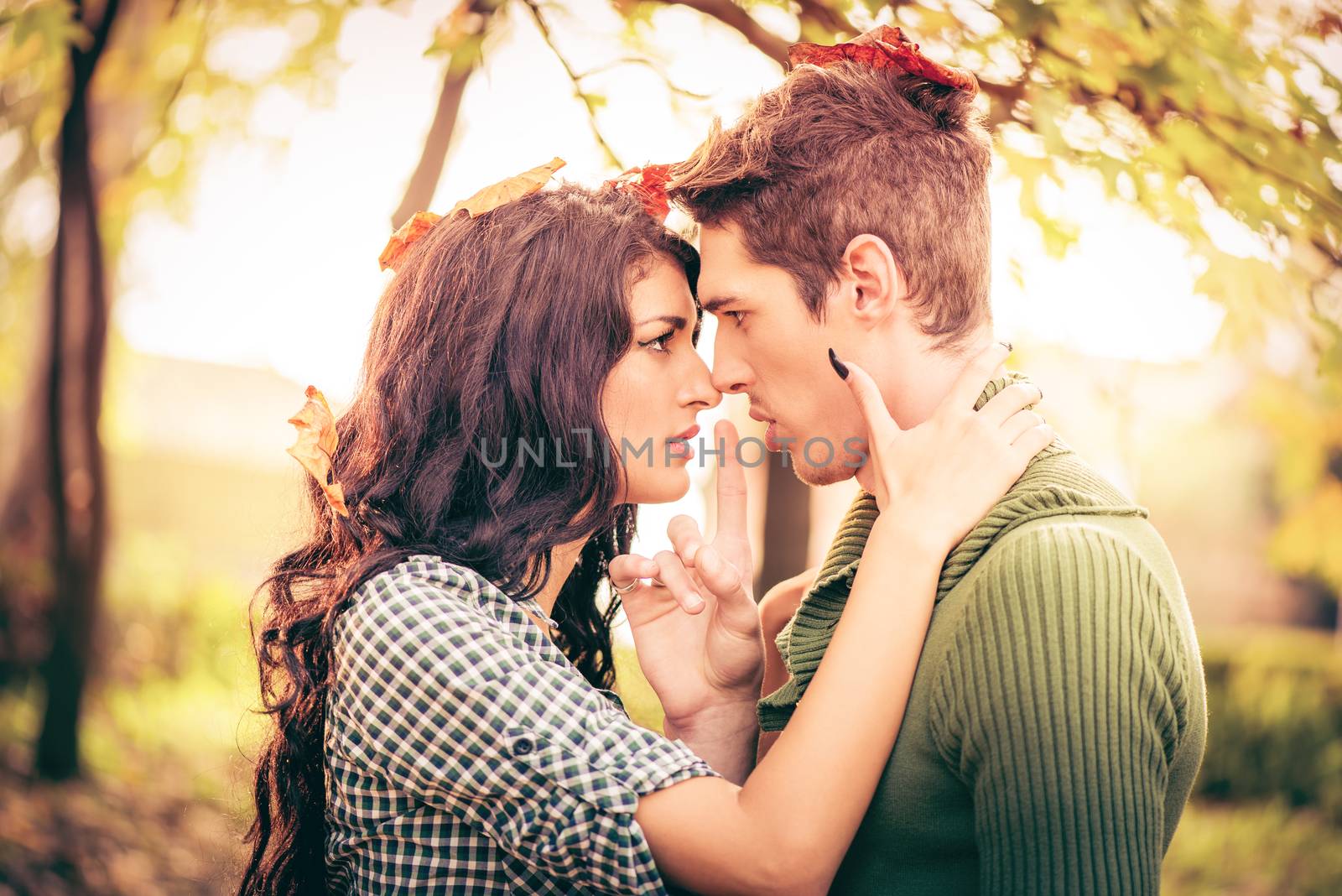 Young heterosexual couple in love in park in the autumn landscape, passionately watch faces turned toward each other, and on their heads were standing fallen autumn leaves.