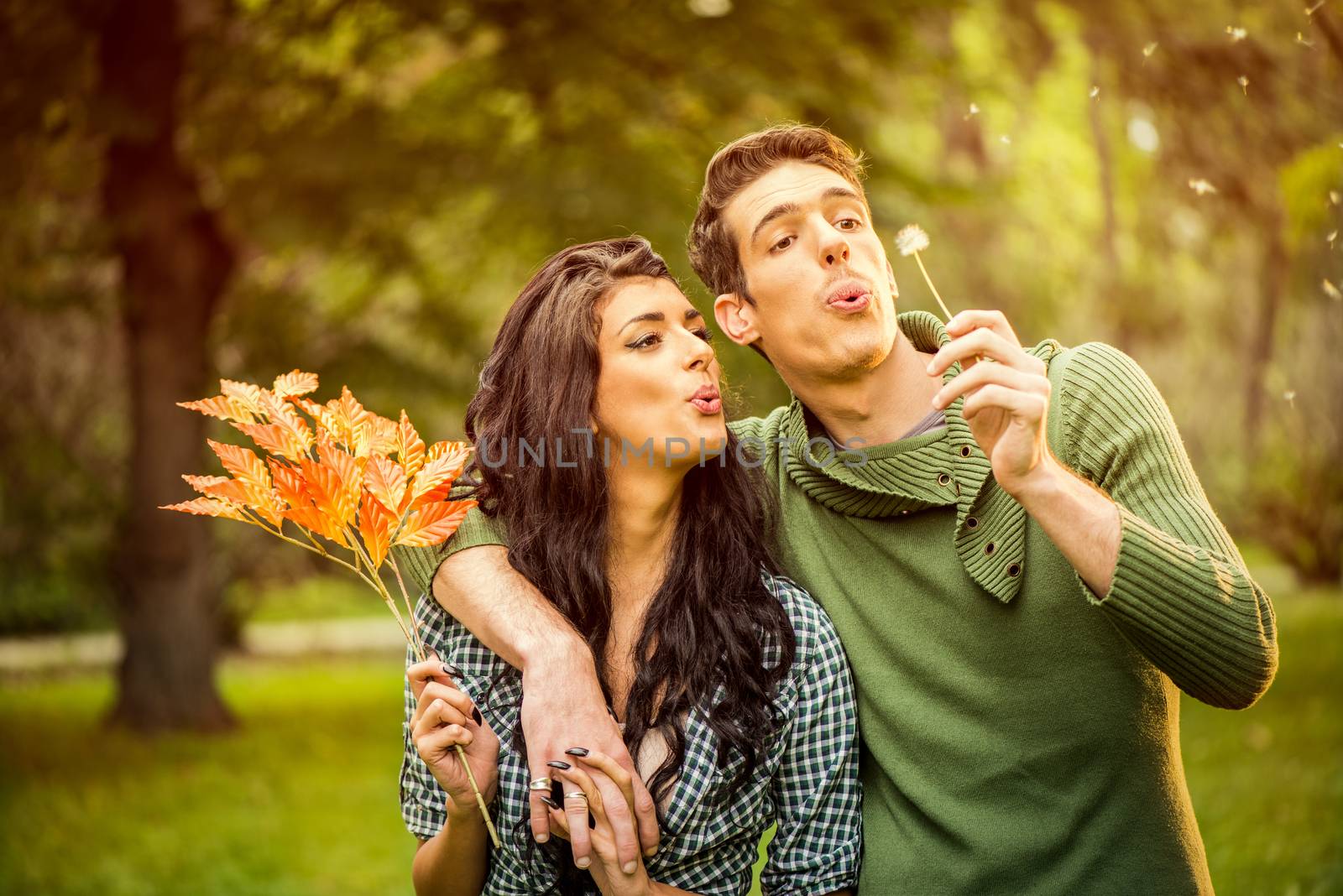 Young heterosexual couple walking in the park, blowing dandelion and holding autumn leaves.