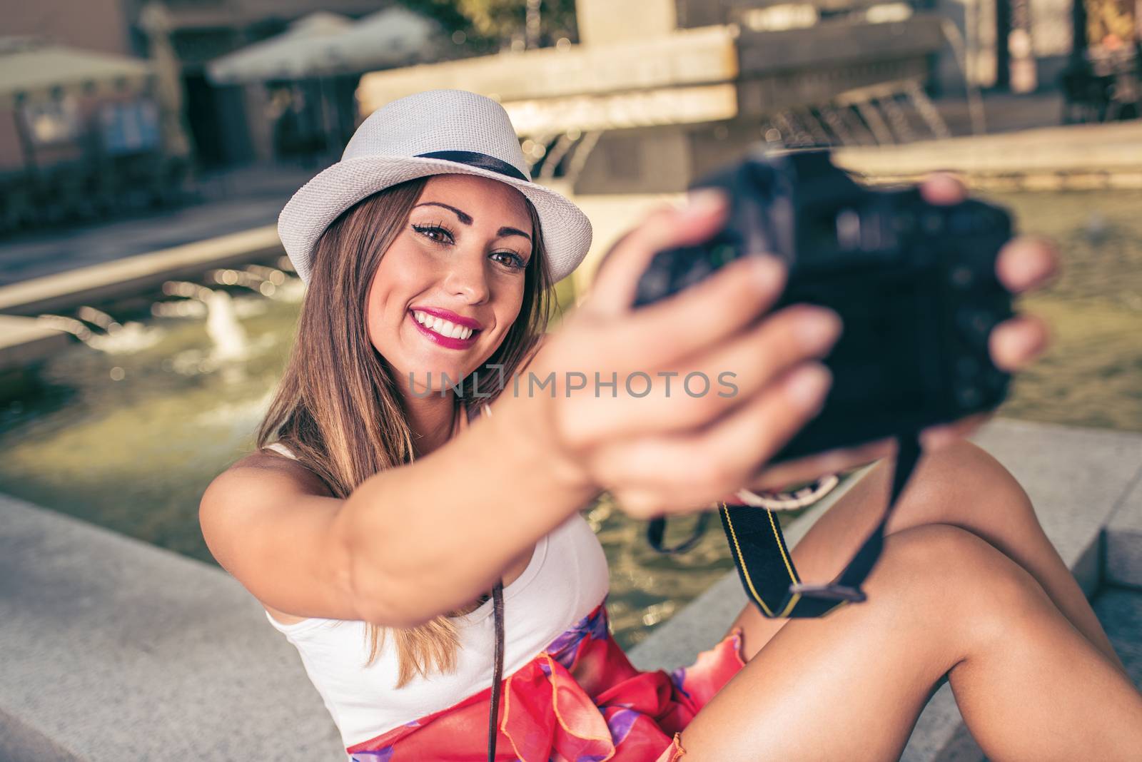 Beautiful young woman on vacation taking selfie in the city square next to the fountain.
