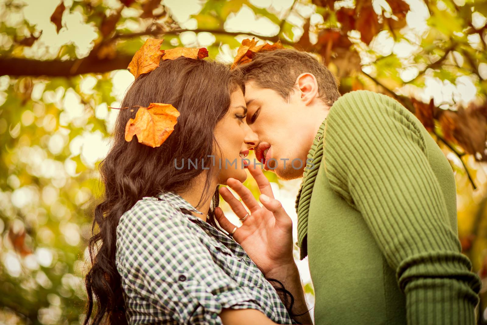 Close-up kiss of a young heterosexual couple in love in the natural environment, while the sun shines through the trees.