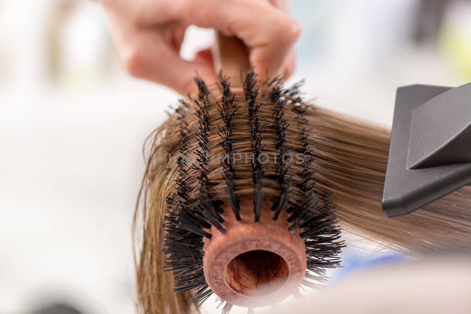Close-up of a drying brown hair with hair dryer and round brush. 