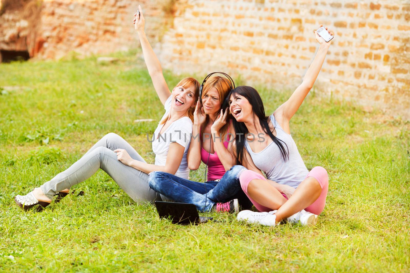 Three young beautiful girls listen music from notebook outdoor