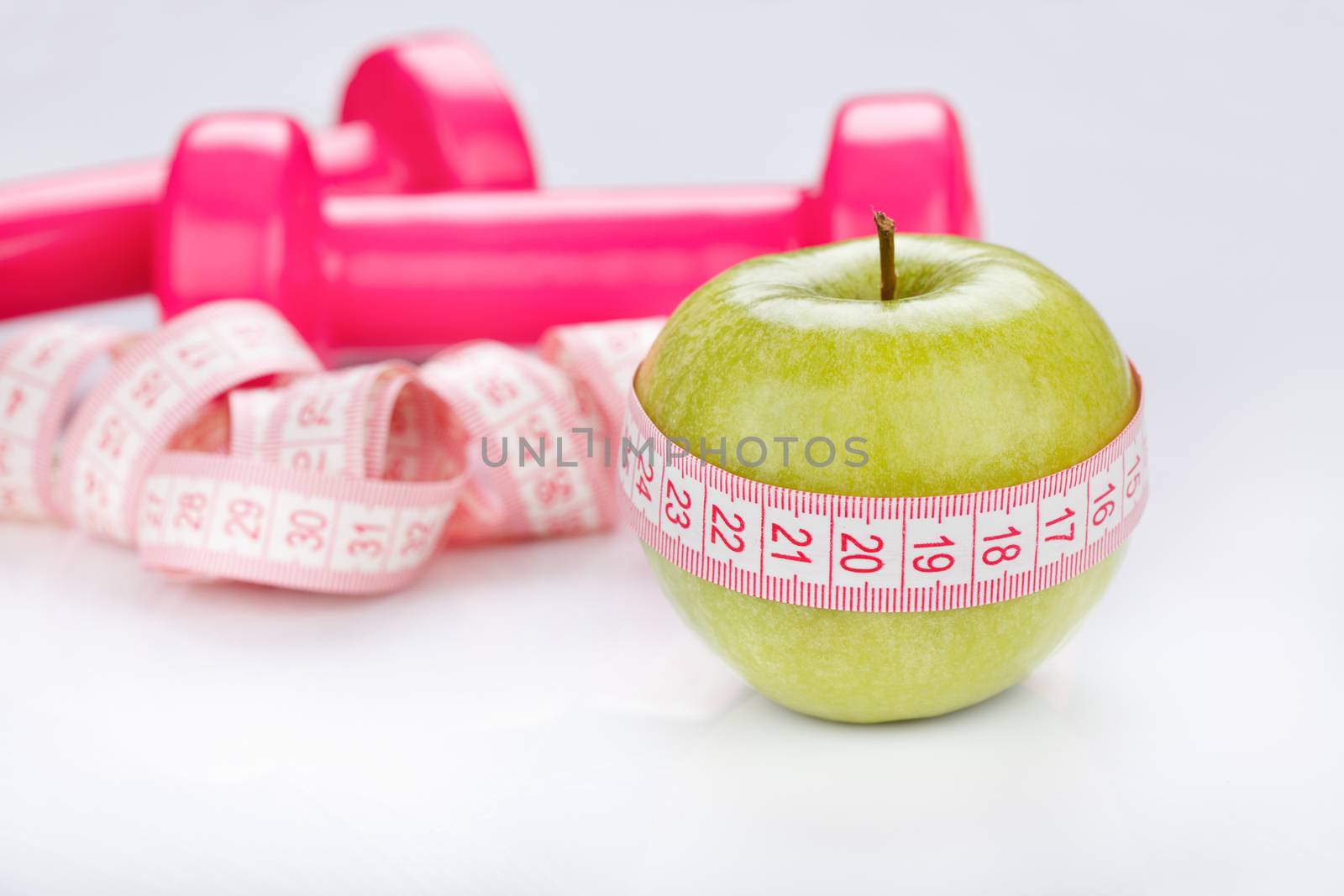 Green apple with a measuring tape around it and pink dumbbells