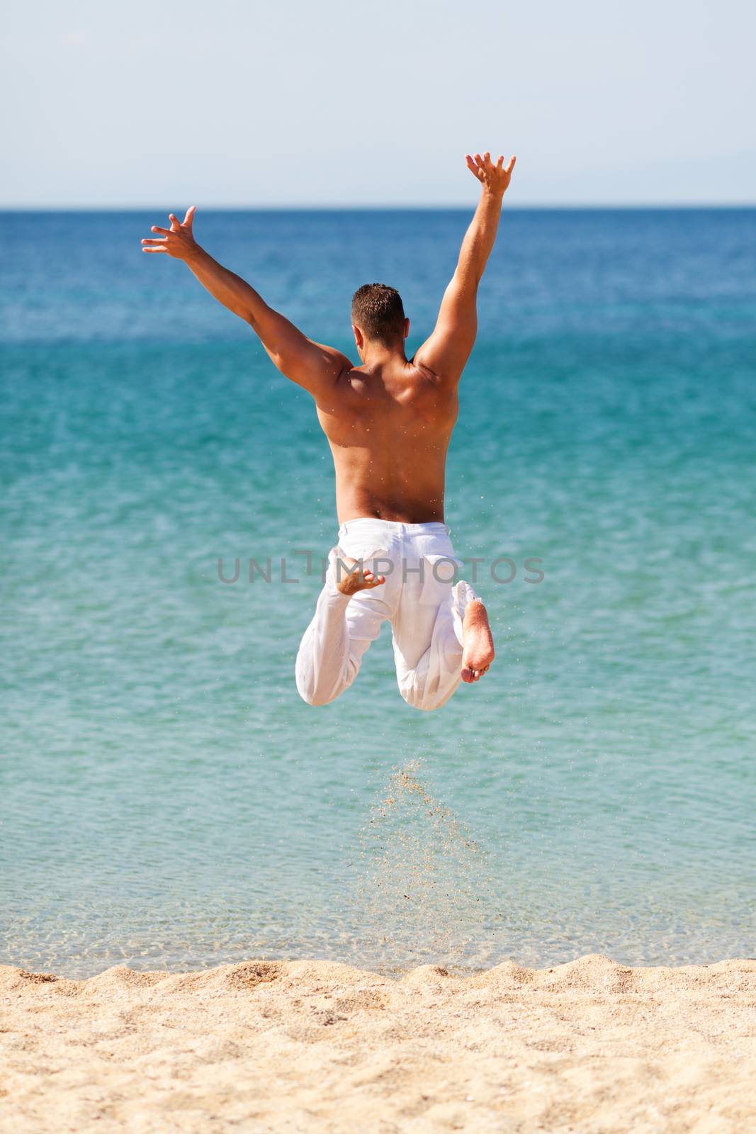 Happy young man in white pants jumping into water