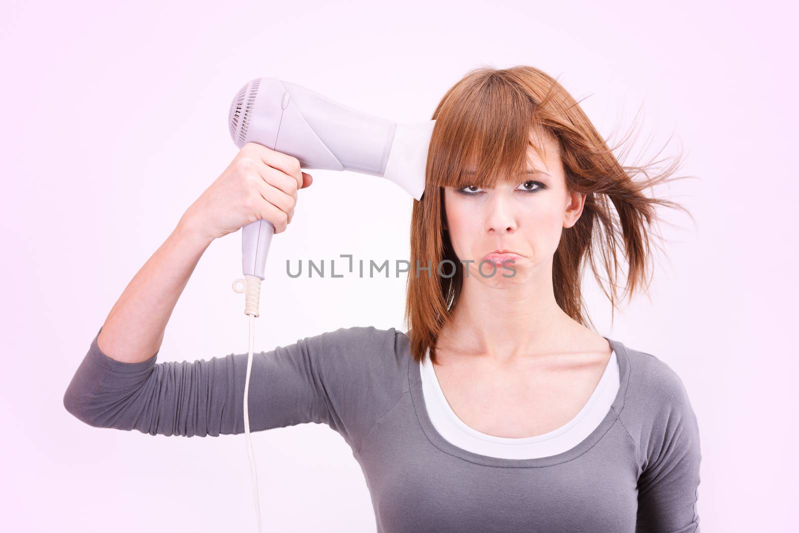 Beautiful young woman holding a hair dryer pointed at head like gun