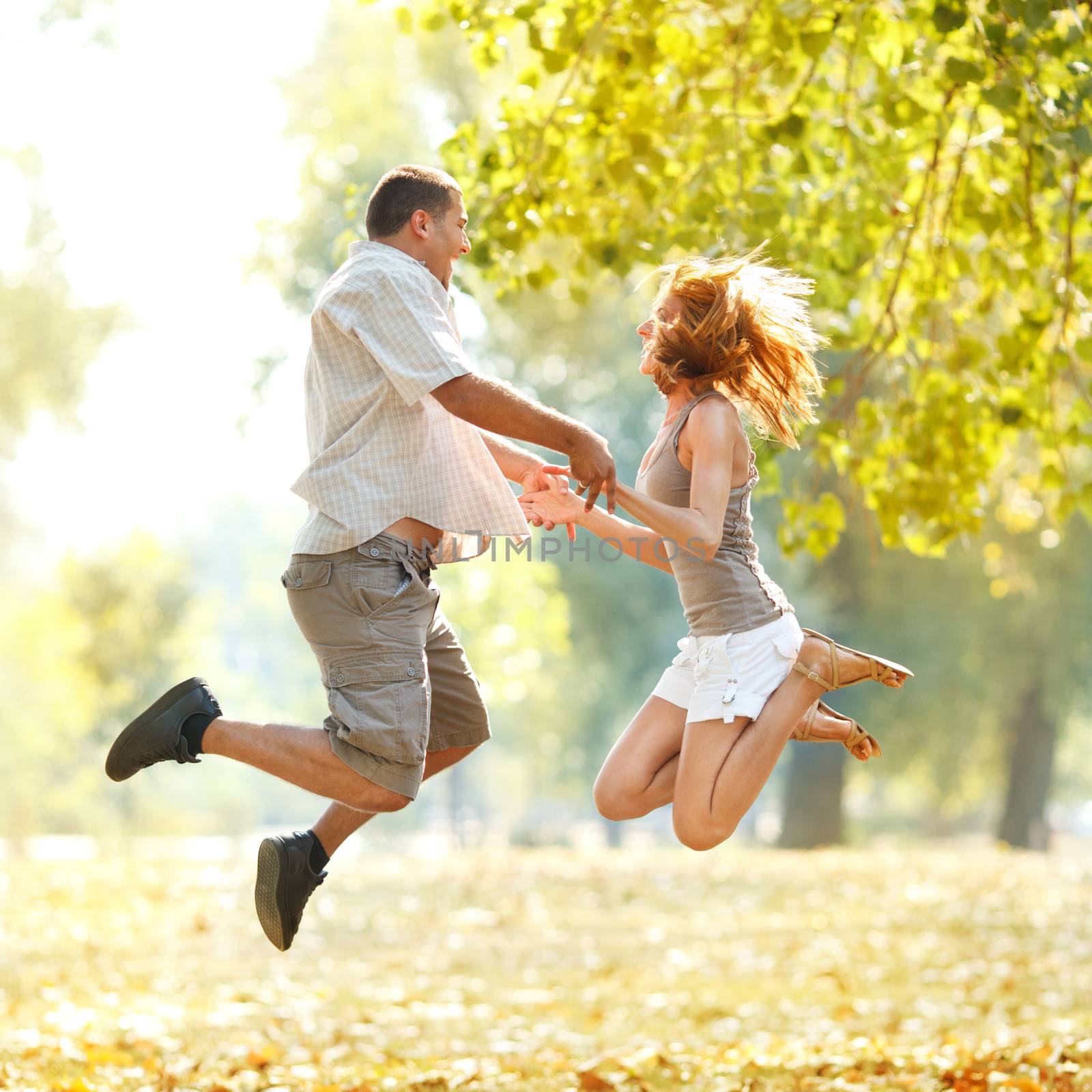 Beautiful happy couple jamping in the park and holding hands