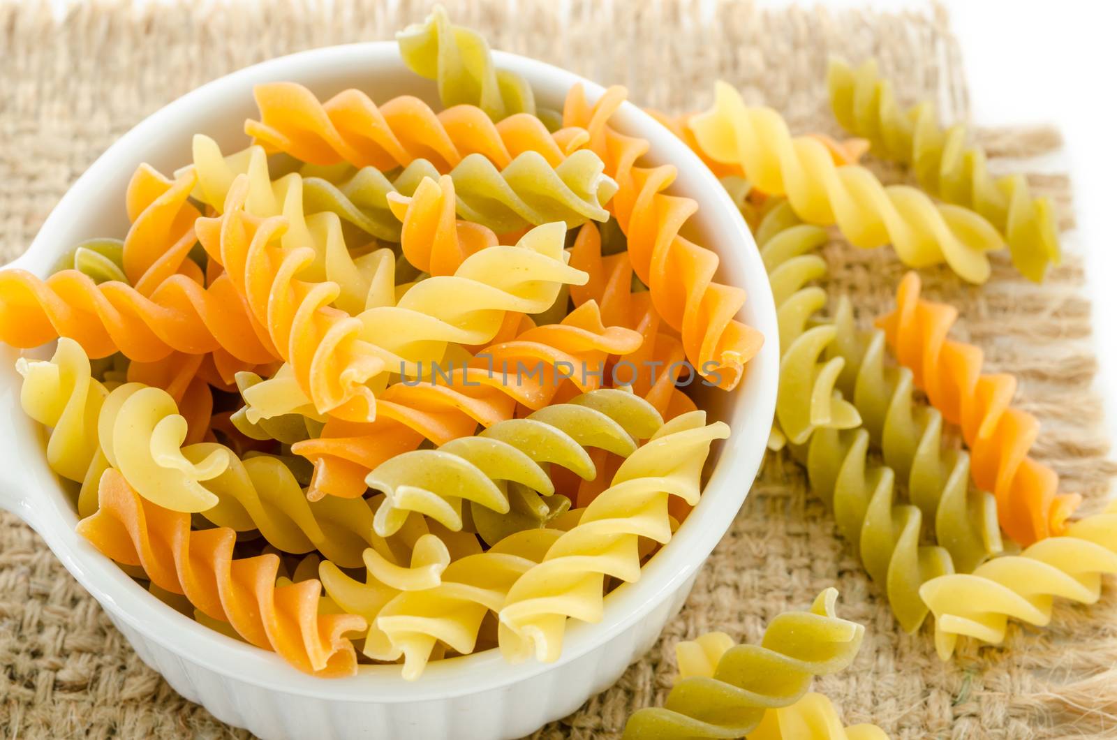 dried italian pasta (macaroni) in white bowl on sack background.