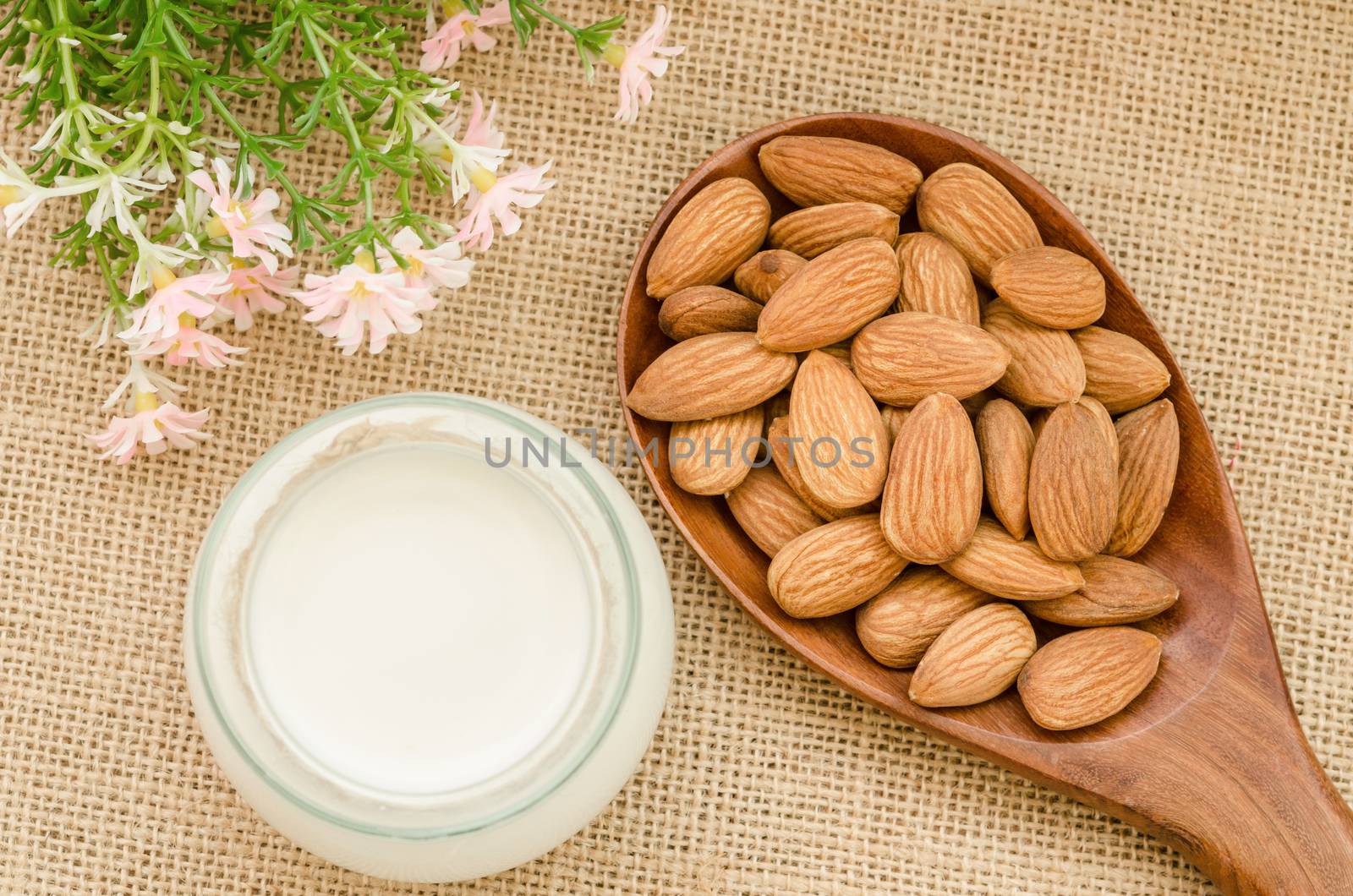 Almond milk with almond on a wooden spoon with flower on sack background.