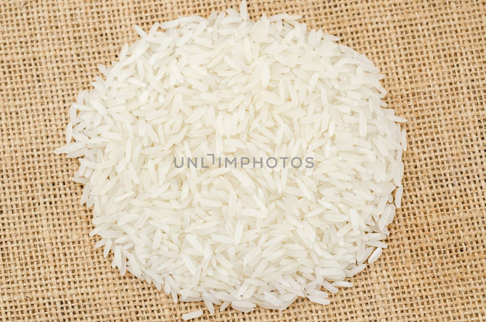 Heap of raw white rice on sack background.