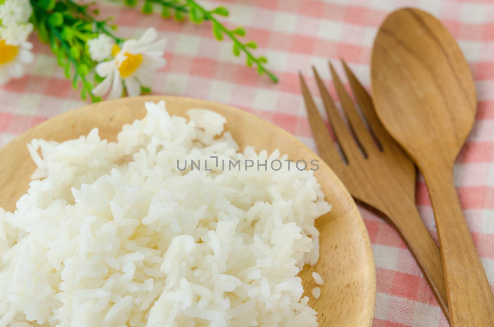 Bowl of Cooked Rice and wooden spoon with flower on tablecloth.