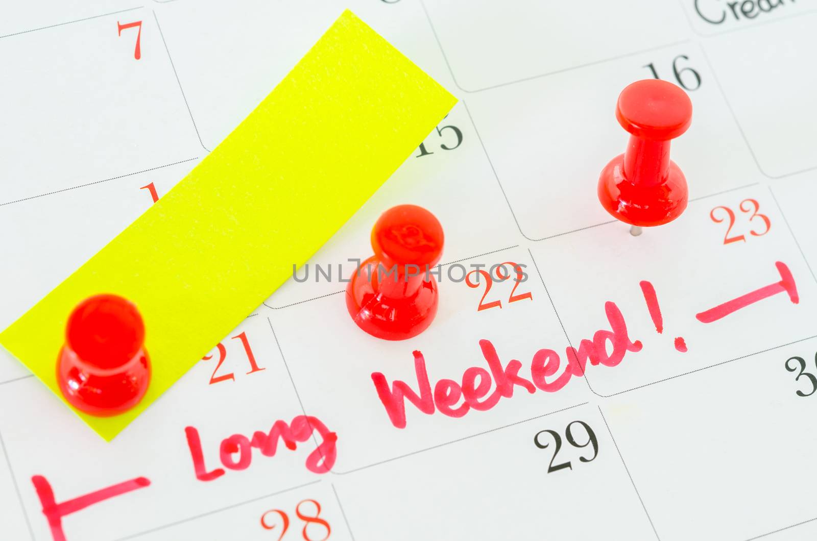 Concept image of a Calendar with a red push pin. Closeup shot of a thumbtack attached. The words Long Weekend written on a white calendar to remind you an important appointment.