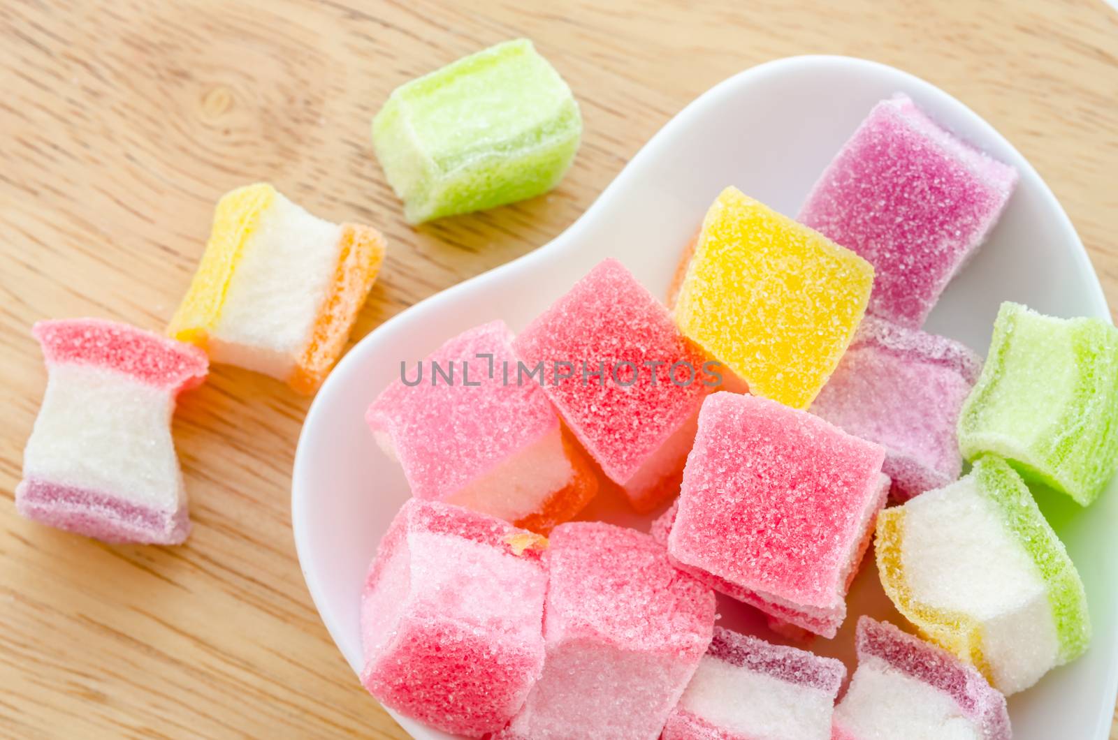 Colorful sweet jellies with sugar in white bowl heart shape on wood background.