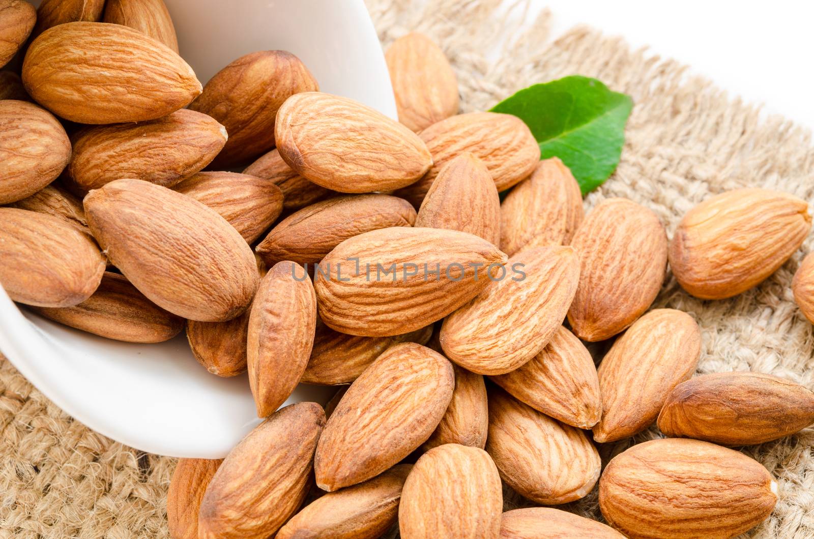 Almonds in white bowl with green leaf on sack.