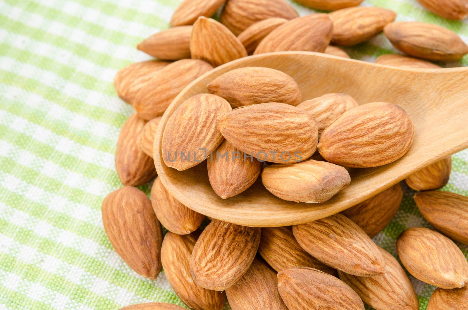 Almonds in wooden spoon on tablecloth.