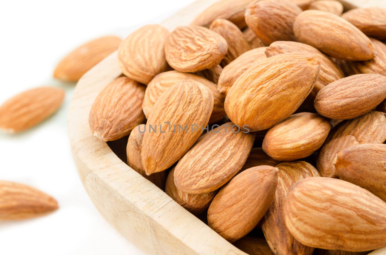 Almonds in wooden bowl on white background.