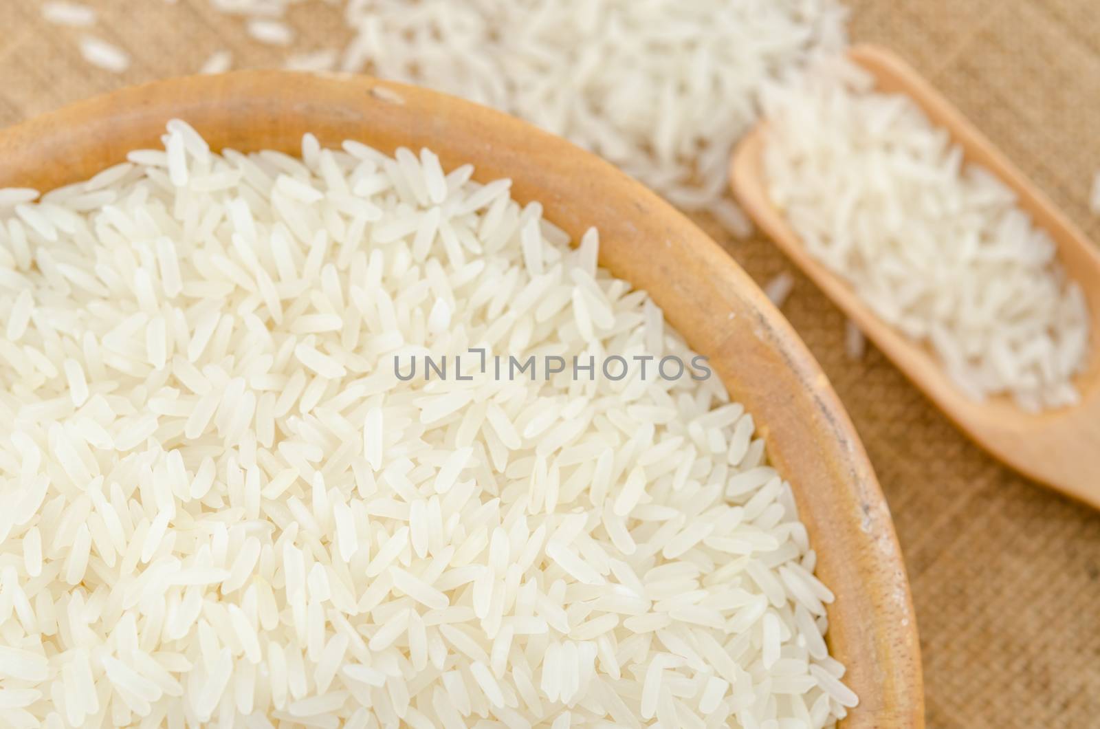Raw white rice in wooden bowl on sack background.