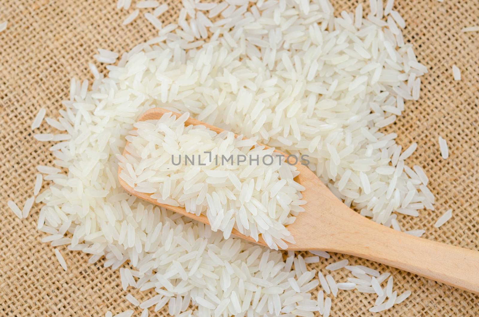 Raw white rice in wooden spoonl on sack background.