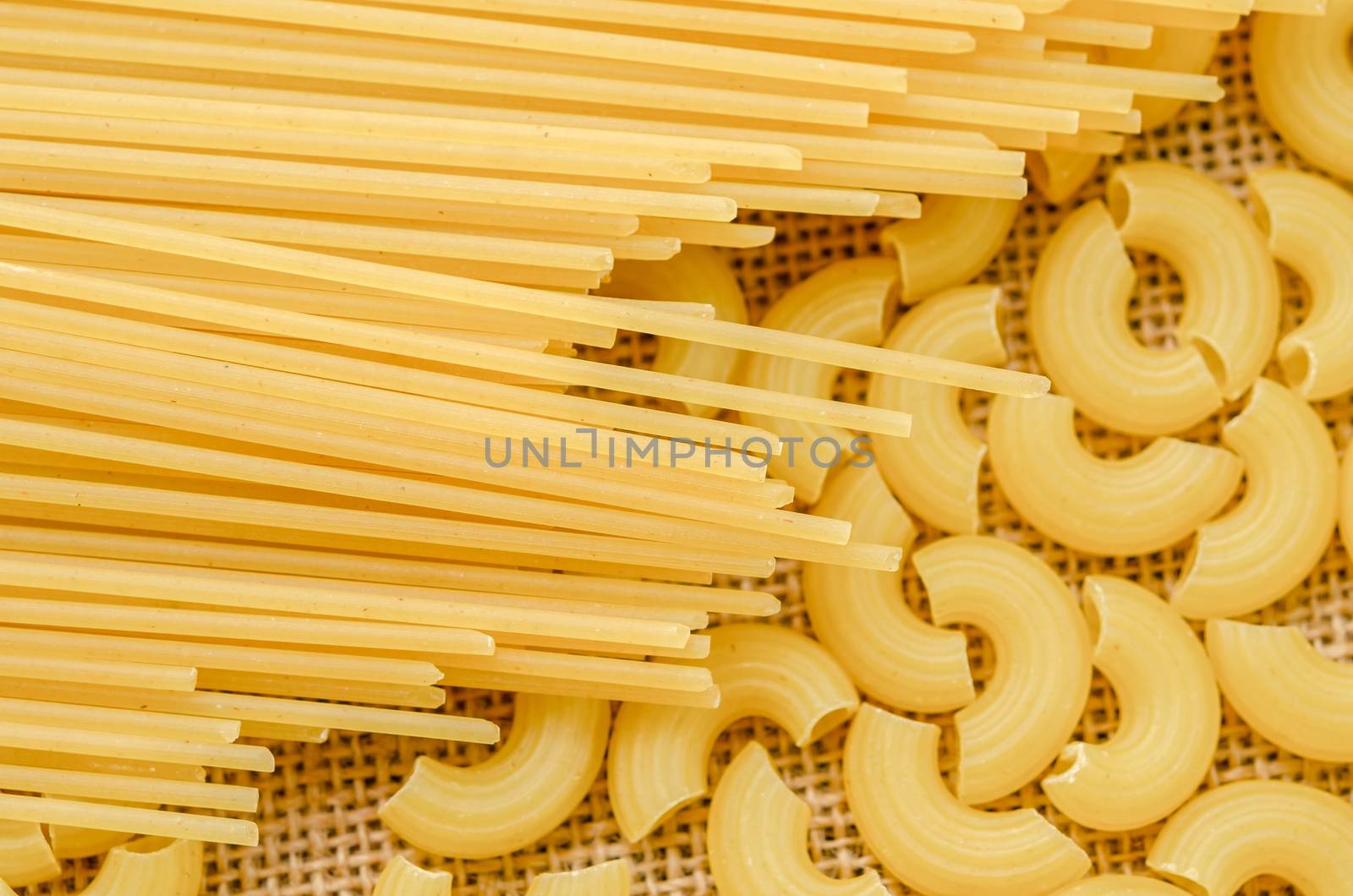 Raw spaghetti and Elbow macaroni noodles on sack background.