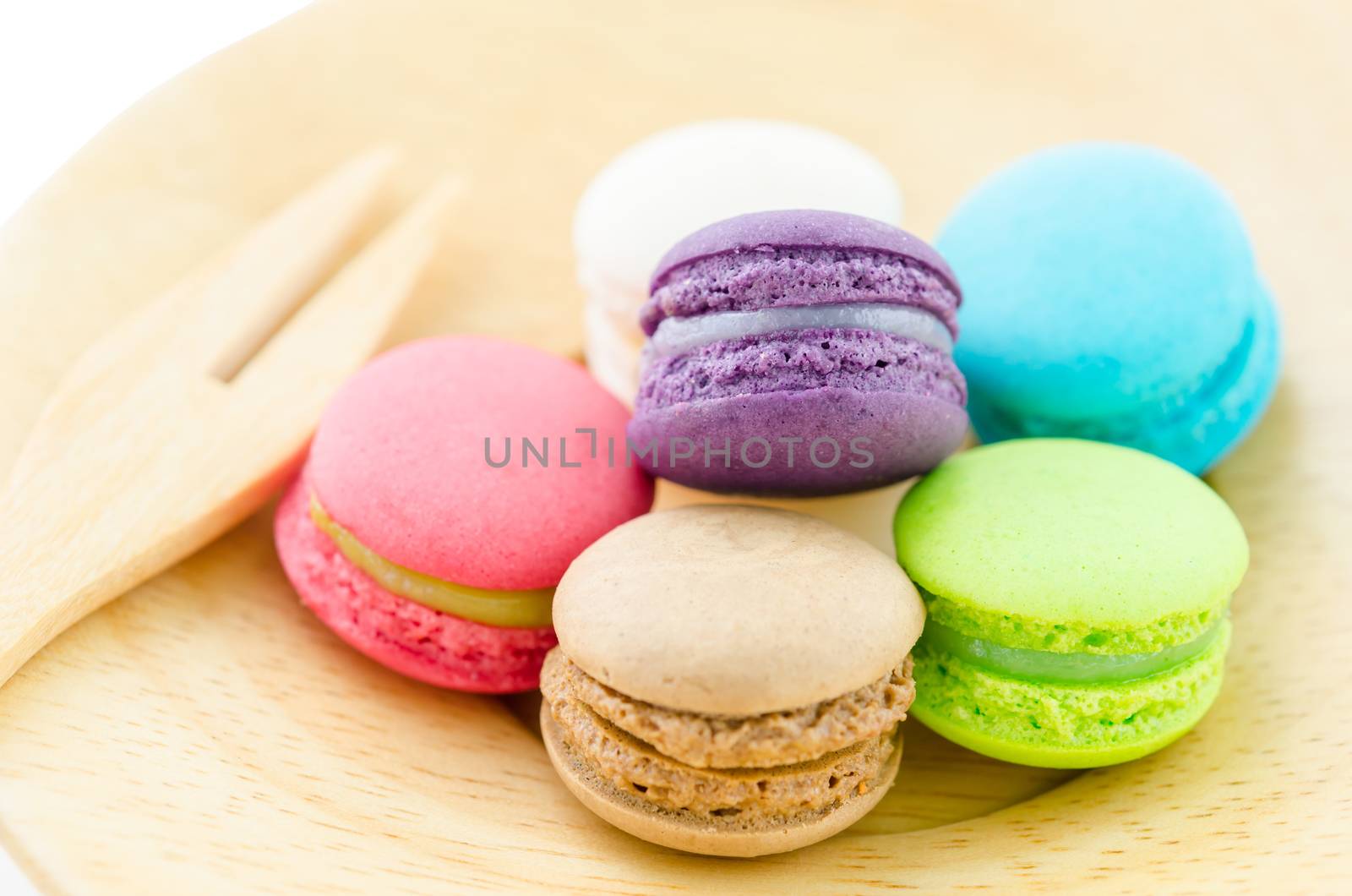 Colorful macaroons in wood dish and wooden fork on white background.