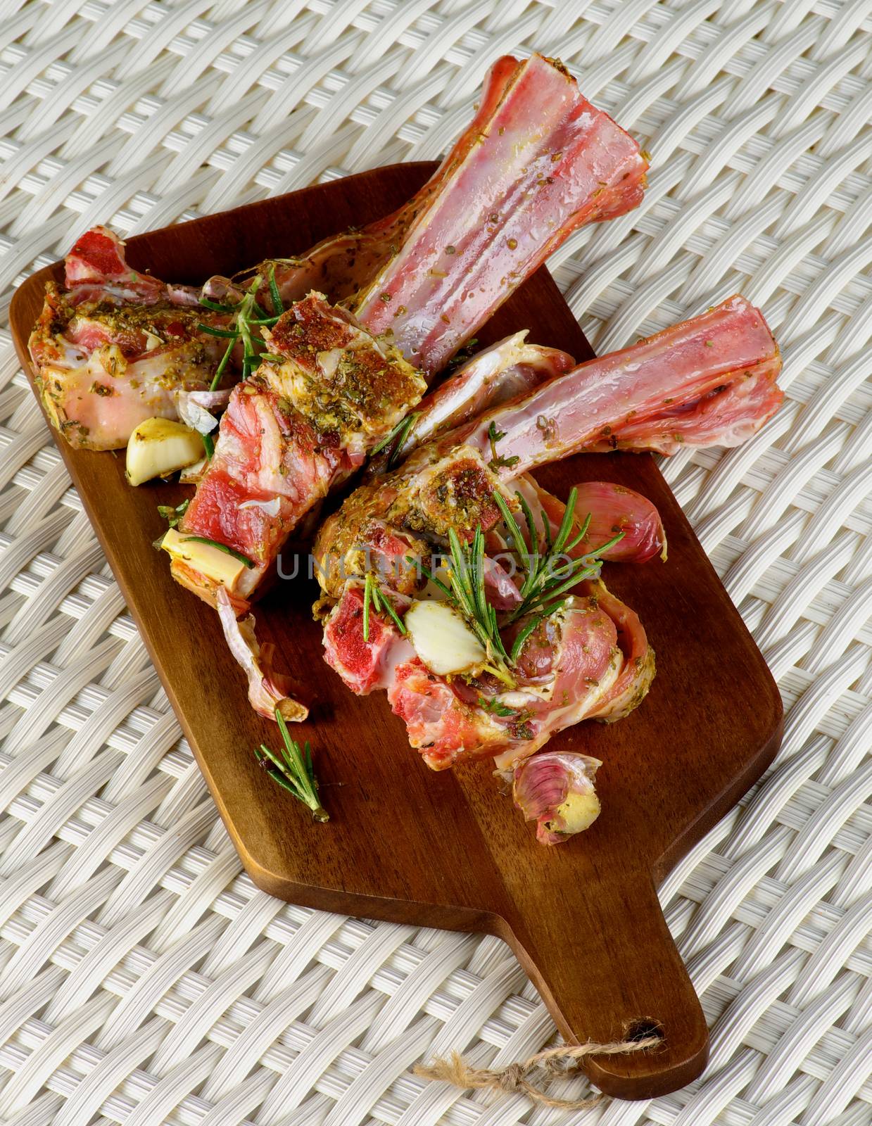 Delicious Raw Lamb Ribs in Marinade of Herbs and Spices with Rosemary and Garlic closeup on Wooden Cutting Board closeup on Wicker background