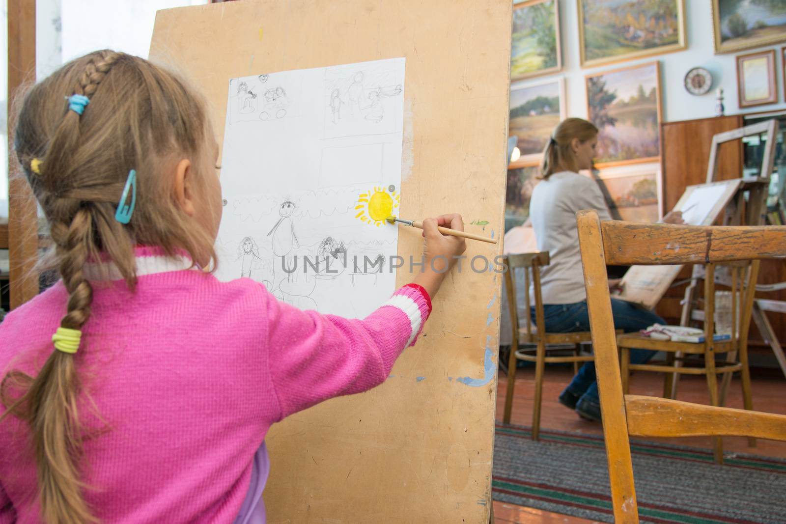 Five-year girl with a brush paints a picture on an easel and holding in his other hand in the artists palette