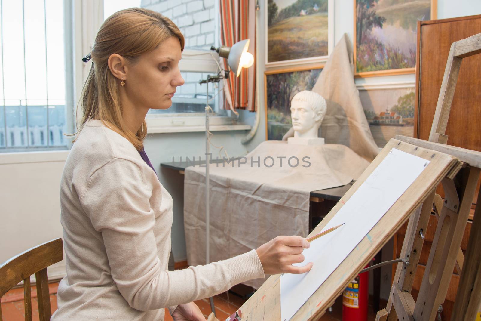A young girl draws a pencil on the easel with a portrait sculpture in the artists studio