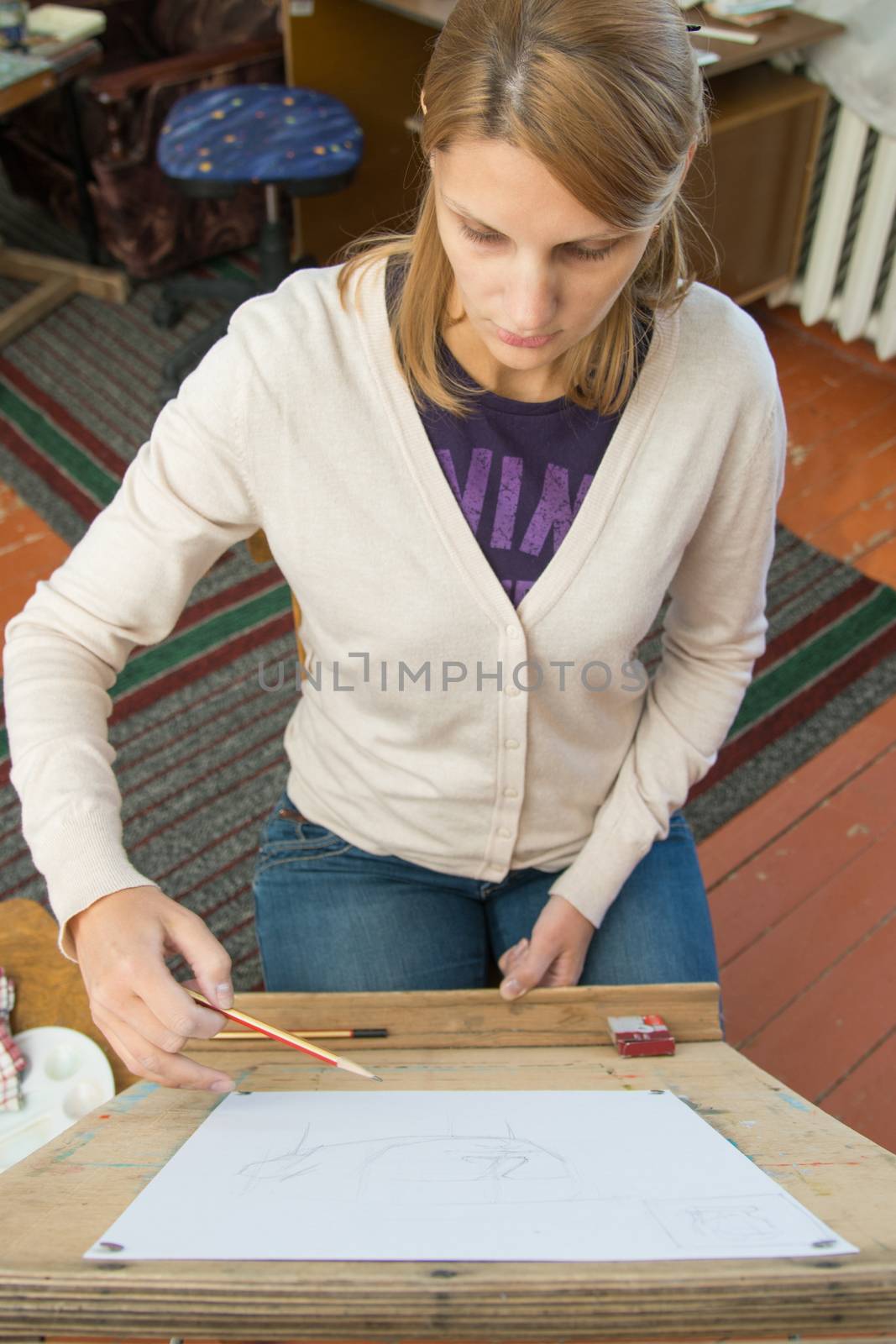 A young girl draws a pencil on the easel with a portrait sculpture in the artists studio