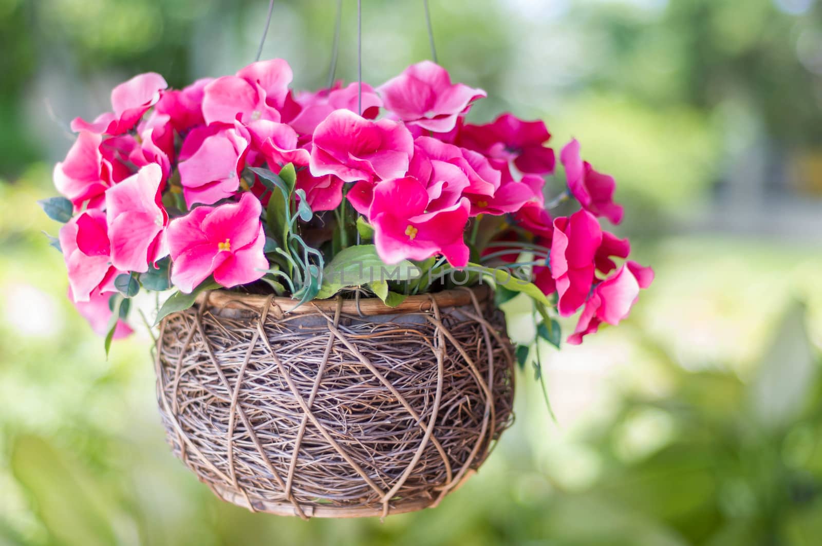 bouquet of artificial flowers in wicker vase on green background.