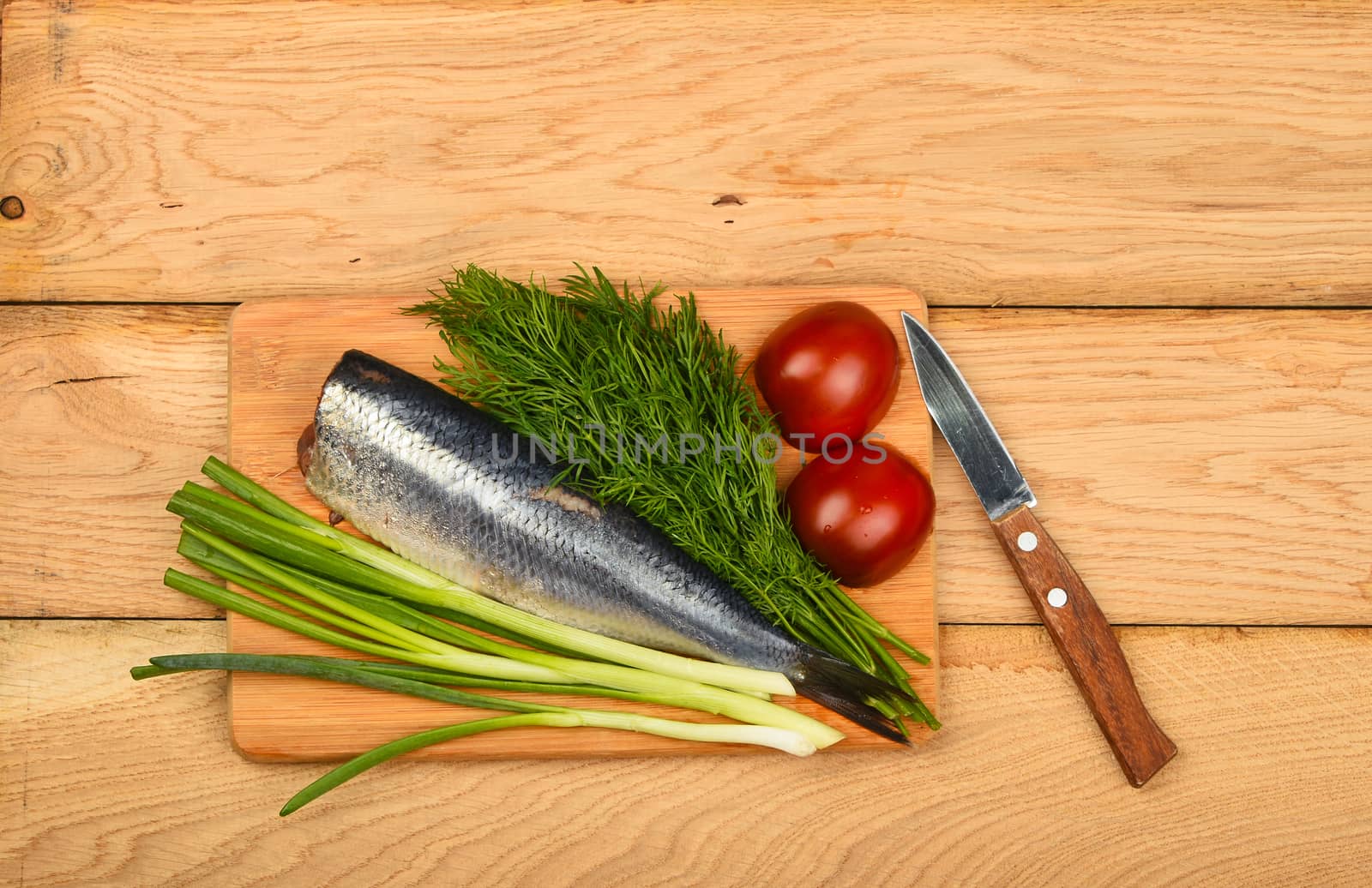 Herring double fillet with onion, dill and tomatoes on bamboo board win small knife on vintage wooden table surface