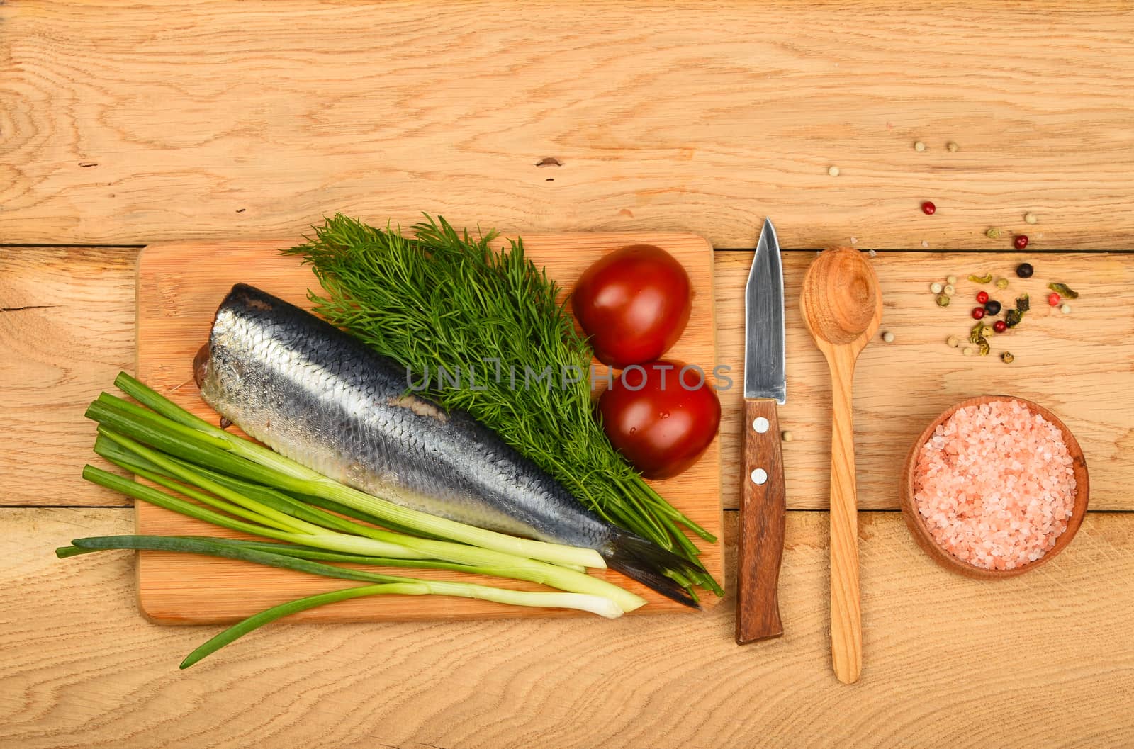 Herring double fillet with onion, dill and tomatoes on bamboo board win small knife, assorted peppercorns, pink salt in wooden scoop on vintage wooden table surface