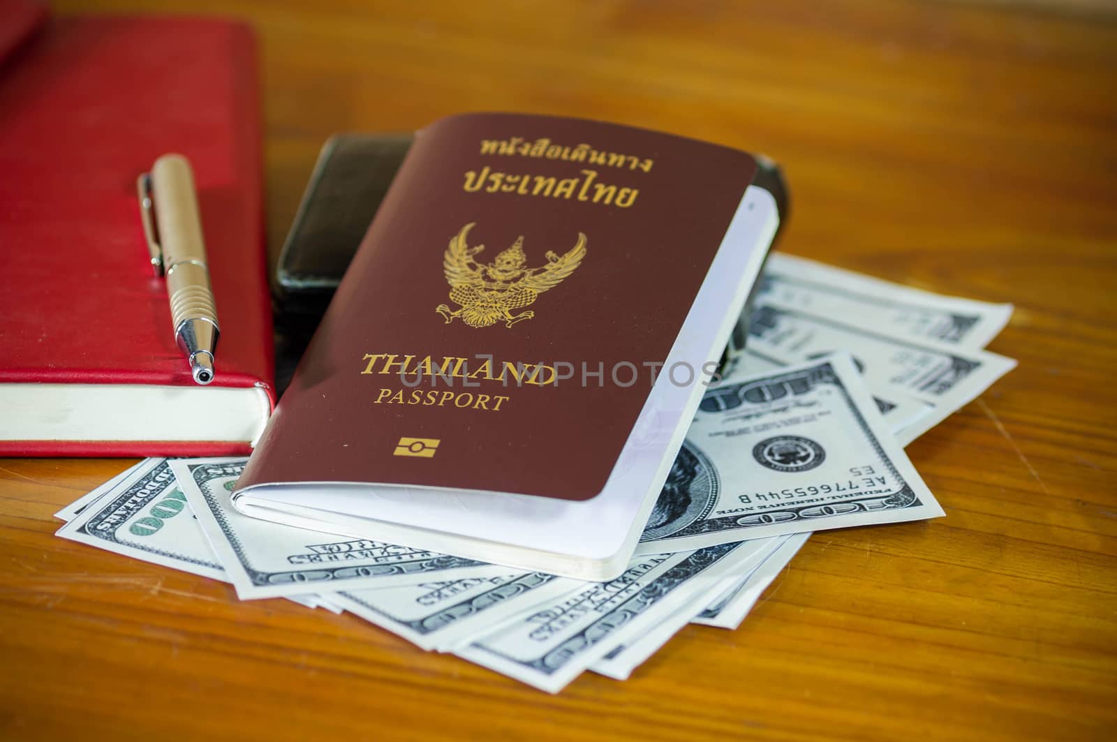 Thailand passport laying atop a pile of American dollars.Note book.
